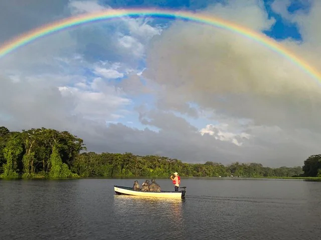 boat with passengers on a river under a vibrant rainbow